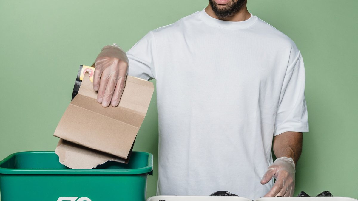 Persona separa cartón en un contenedor de reciclaje.
