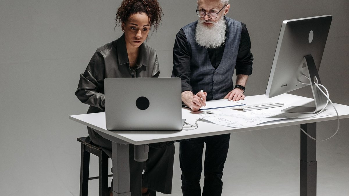 Dos profesionales trabajan de pie frente a un escritorio con computadores.