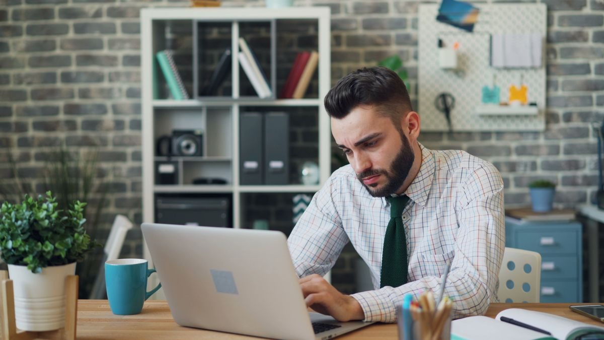 Profesional de camisa y corbata trabaja solo frente a un notebook en una oficina.
